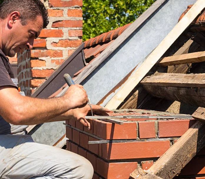 Mason striking joints on a new brick chimney beside a Pasadena roof